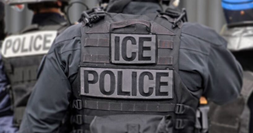 An ICE officer in his uniform stands among his colleagues.