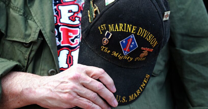 A veteran marine holds his commemorative hat on top of his heart.