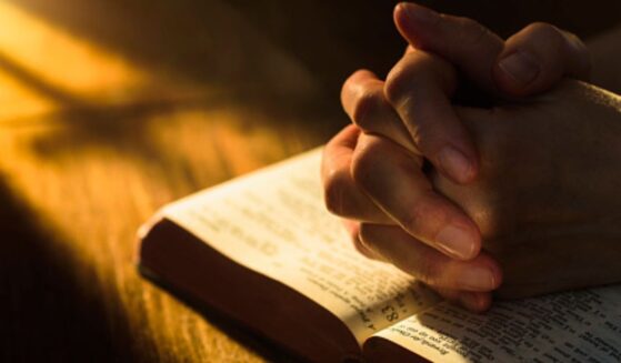 Hands clasped in a prayerful position over an open Bible.