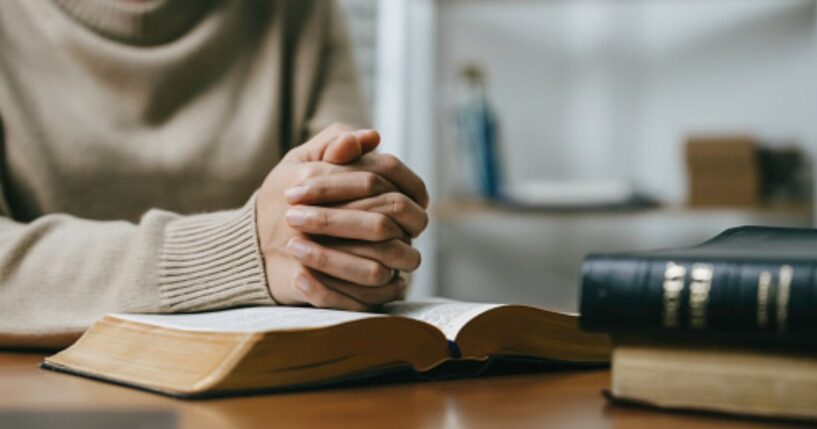 Woman prays with her hands on a Bible.