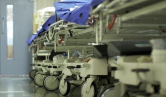 A hospital hallway is filled with gurneys and trolleys lined up on the wall.