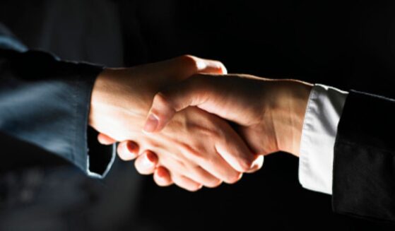 Two men shake hands in a dark room.
