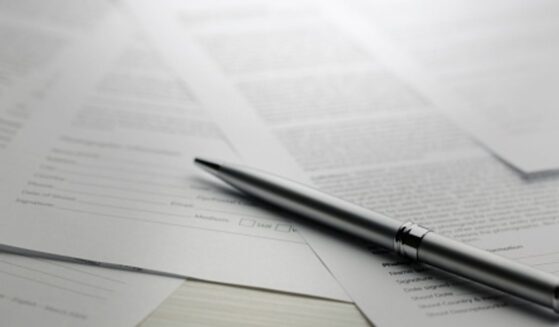 Papers are strewn across a table with a pen laying on top of them all.