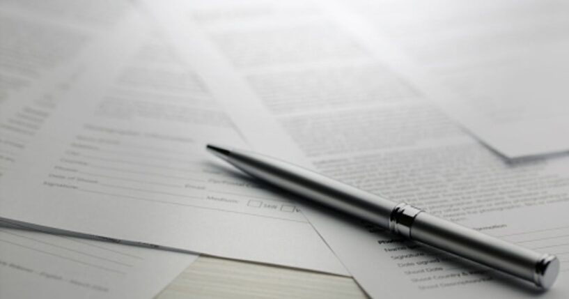 Papers are strewn across a table with a pen laying on top of them all.