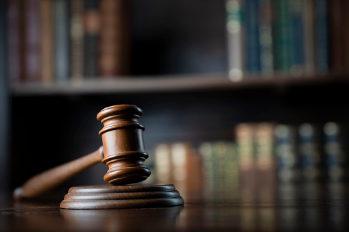 A gavel and wooden block sit on a table while book shelves sit behind them.