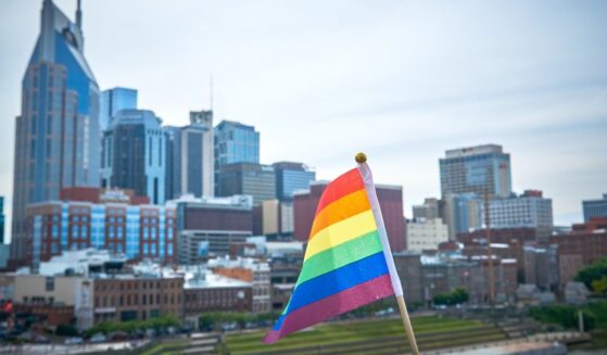 A rainbow flag flies in the foreground with the city of Nashville in the background.