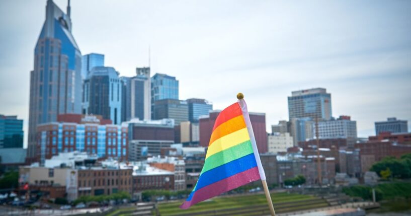 A rainbow flag flies in the foreground with the city of Nashville in the background.