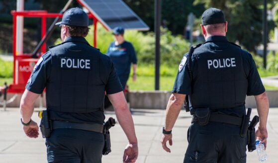 Police officers walk through a city park in the daylight.