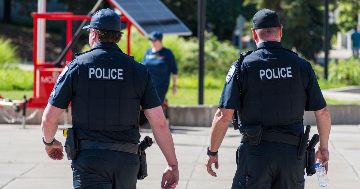 Police officers walk through a city park in the daylight.