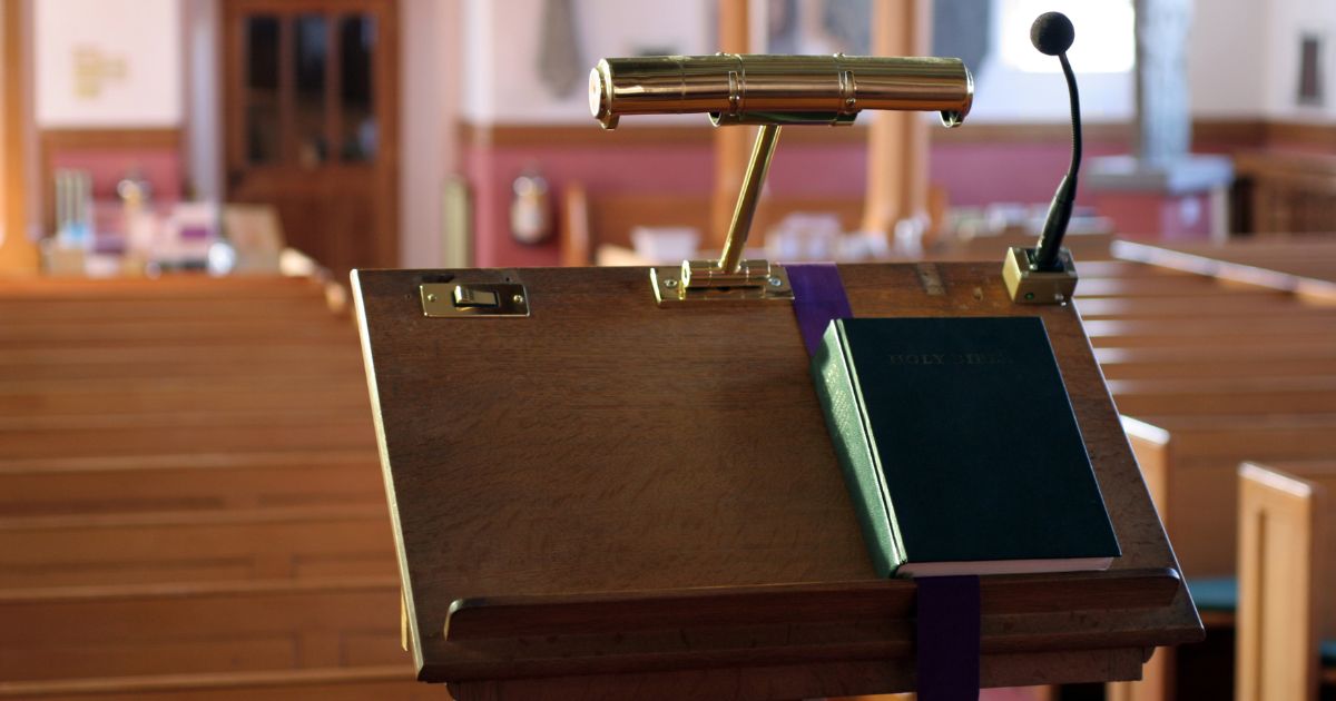 A modern wooden church pulpit with a light, microphone, and Bible on it.