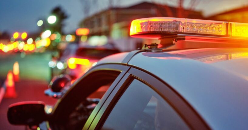 A police car sits alongside a road at night while its lights are flashing.