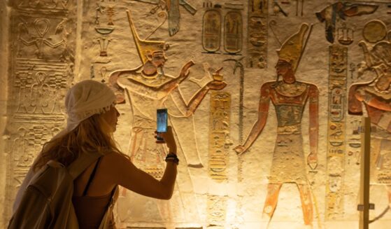 A woman holds out her smartphone and takes a picture of ancient depiction of Ramses IX at the Valley of Kings in Luxor, Egypt.