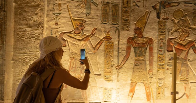 A woman holds out her smartphone and takes a picture of ancient depiction of Ramses IX at the Valley of Kings in Luxor, Egypt.
