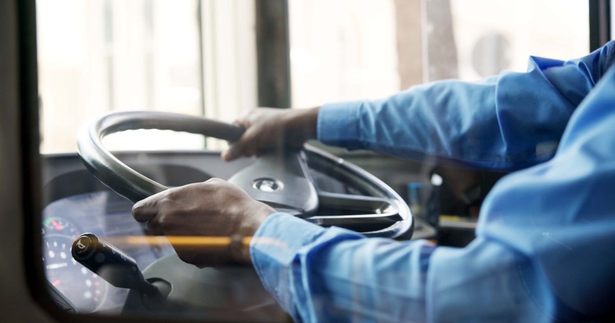 A bus driver holds the steering wheel of the bus with both hands.