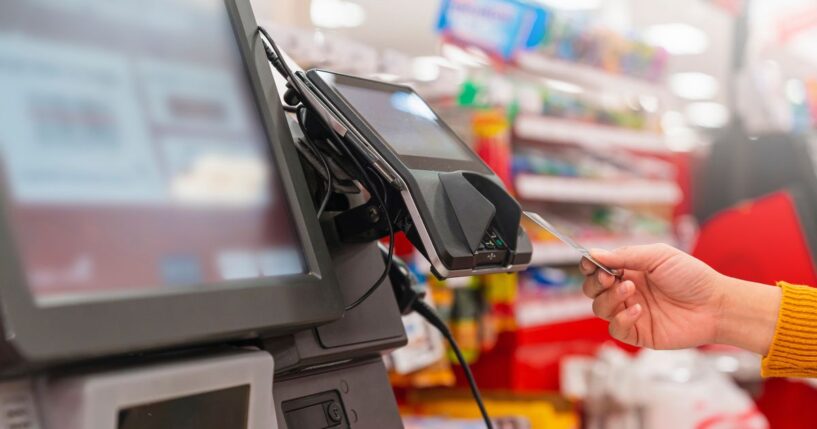 A person uses a card to pay at a grocery store self-service kiosk.