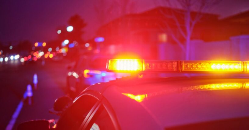 A police car at night alongside a road with emergency lights flashing.