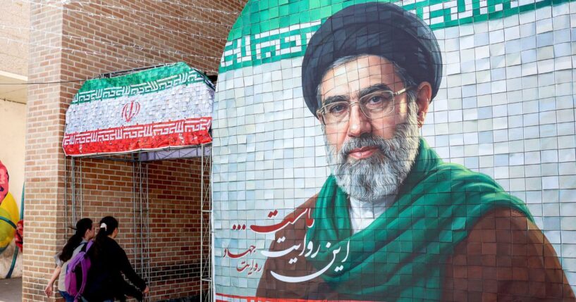 Women walk past a banner depicting Iran's current supreme leader Ayatollah Mojtaba Khamenei along a street Tehran on May 6, 2026.