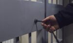 A photo illustration shows a hand using a key to open a barred door.