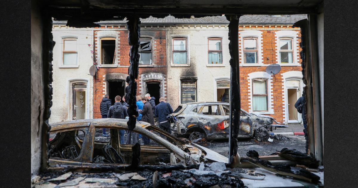 People stand next to burnt-out cars and homes Wednesday after demonstrations turned violent the night before in eastern Belfast, Northern Ireland.