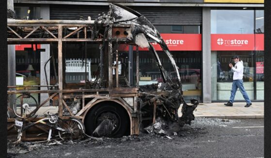 A pedestrian passes a burned-out bus Wednesday following a night of anti-immigrant riots Tuesday in Belfast, Northern Ireland.