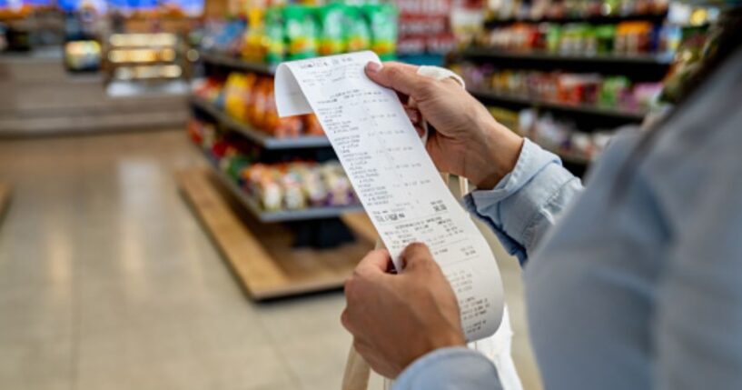 A woman looks at a receipt in a grocery store aisle.