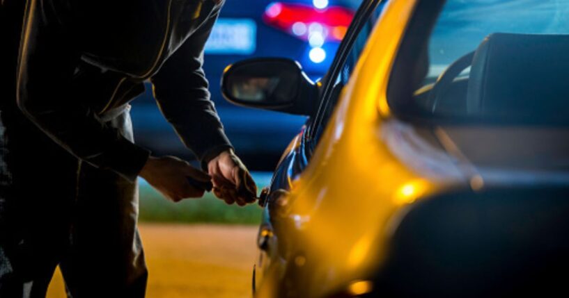 A man tries to pick a lock on a car.