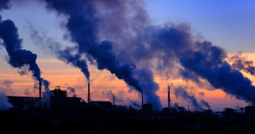 Plumes of smoke cloud from chimneys at dusk.