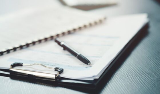 A clipboard, papers, and a pen lay on a black desk.