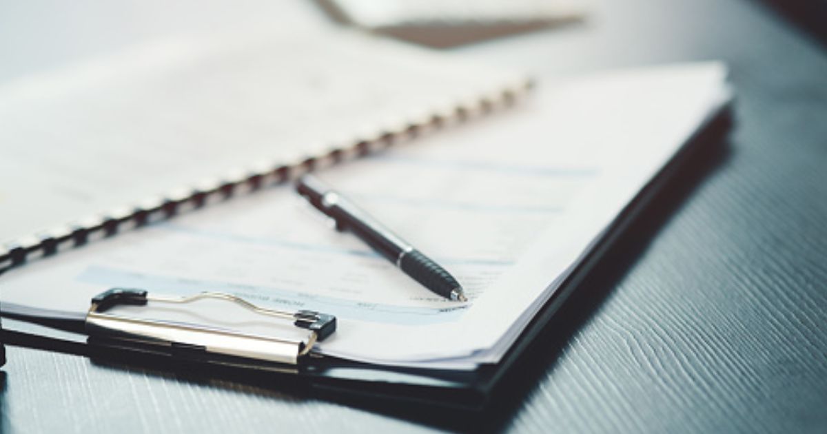 A clipboard, papers, and a pen lay on a black desk.