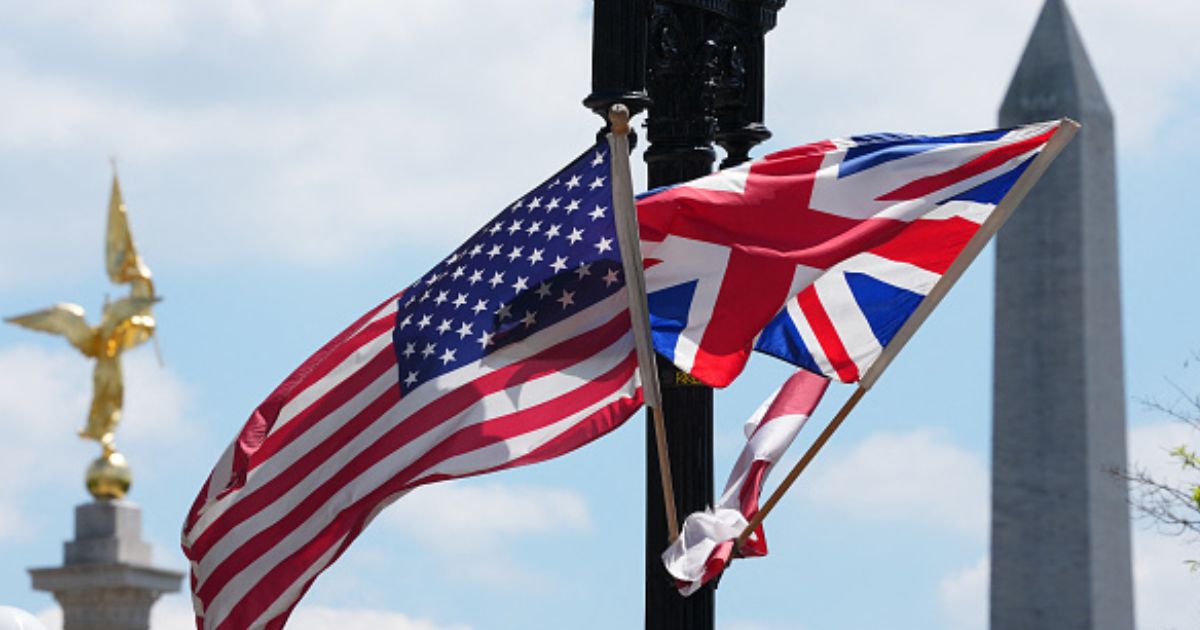 The United States flag and United Kingdom flag wave together on a light pole.