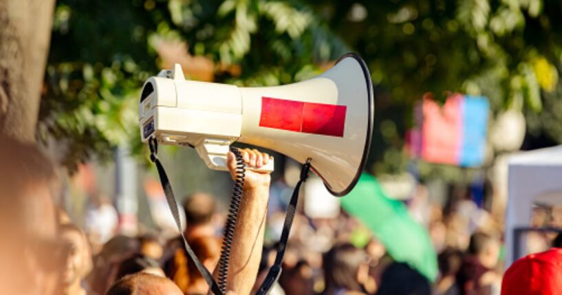 A protestor raises a megaphone amongst a crowd.