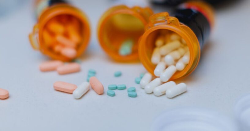 Pill bottles spill multi-colored pills out onto a white table.