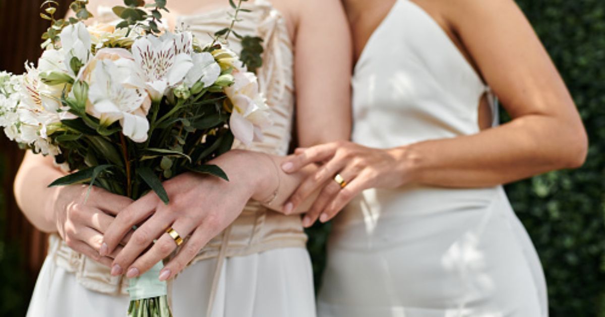 Two women dressed as brides stand close to each other as one embraces the other.