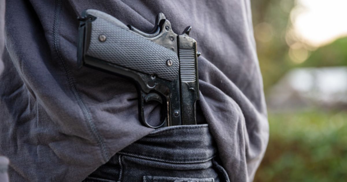 Man carries gun in his pants as he walks in a field.