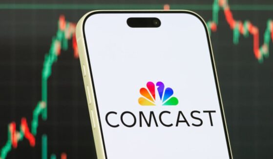 The Comcast logo is displayed on a phone while a stock market depiction is pictured behind.