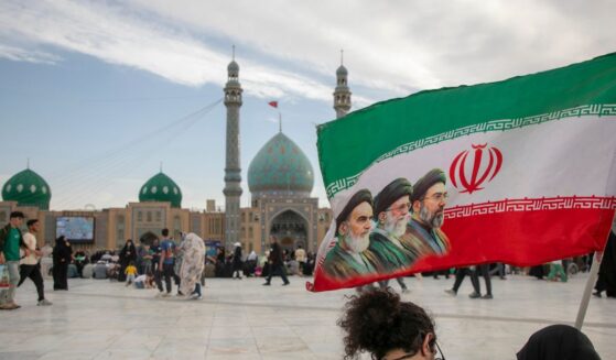 People hold a flag with Iran's late and new supreme leaders, Ayatollah Ruhollah Khomeini, Ayatollah Ali Khamenei, and Ayatollah Mojtaba Khamenei, during Eid al-Adha at the entrance of Jamkaran Mosque on May 26, 2026, in Qom, Iran.