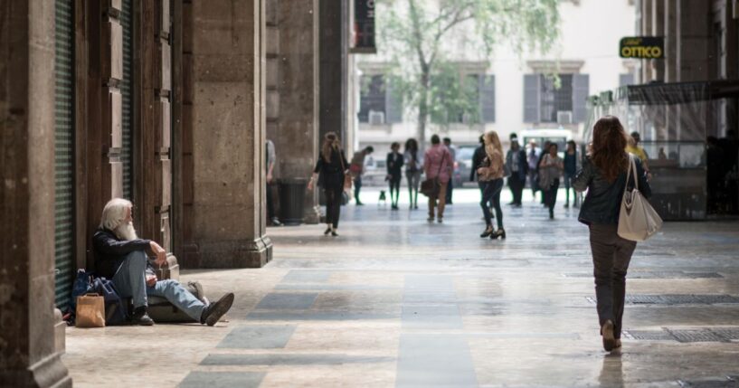 A homeless man sit in the street watching people passing by in Milan, Italy, on May 7, 2015.
