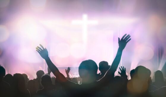 Christians raising their hands in praise and worship with a cross in the background.