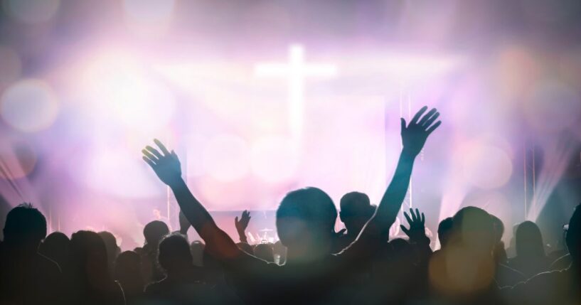 Christians raising their hands in praise and worship with a cross in the background.