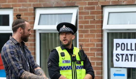 A police officer stands on duty as people arrive to cast their vote in the Makerfield by-election, at a polling station set up at a Library in Winstanley, part of the Makerfield parliamentary constituency, in northwest England on June 18, 2026.