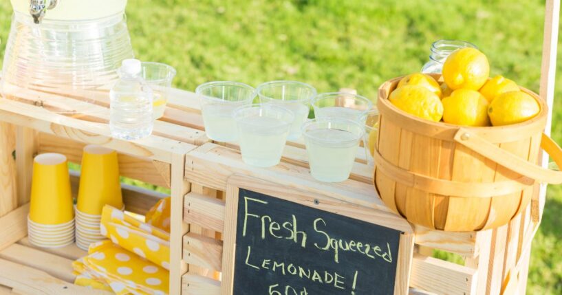A lemonade stand is set up in the front yard of a home in the suburbs.