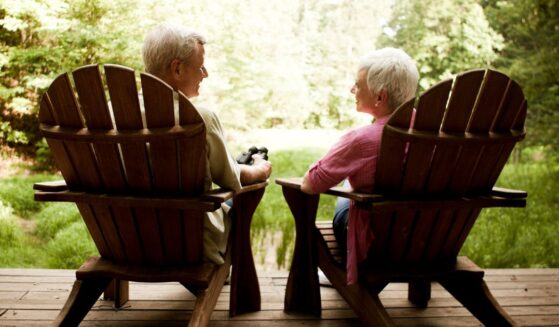 The rear view of a senior couple relaxing in Adirondack chairs on a wooden deck.