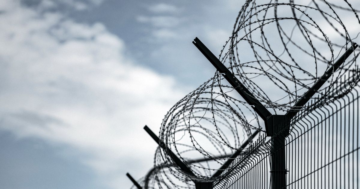 A prison with razor wire against a dark sky.