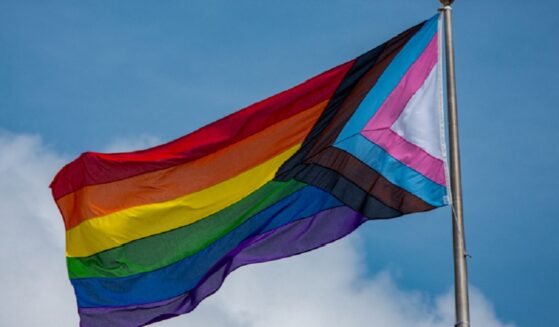A rainbow flag flies against a blue sky.