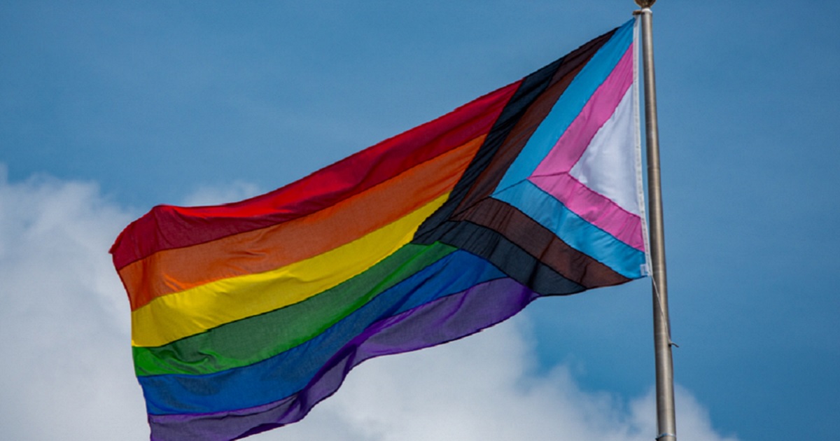 A rainbow flag flies against a blue sky.