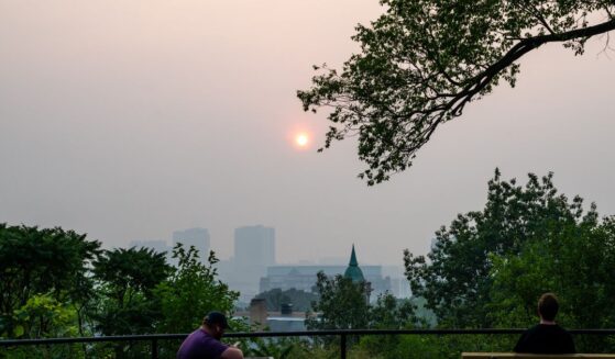 People look on as the sun sets behind a layer of smoke on July 15, 2026, in Minneapolis, Minnesota.