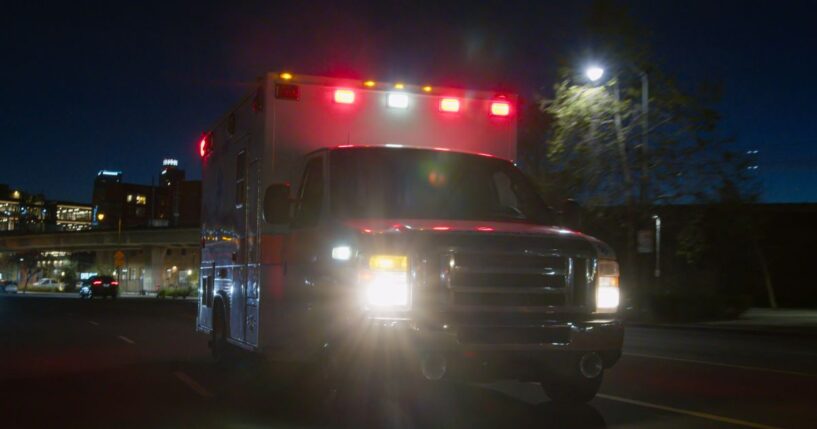 An ambulance driving through a downtown district at night.
