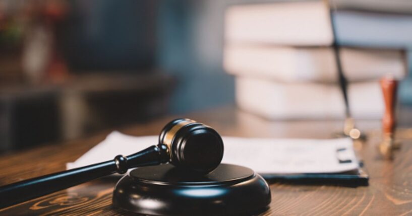 A black wooden gavel sits on a black wooden block in a bright room.