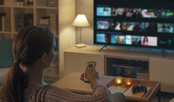 A young woman turns on the television in her living room.