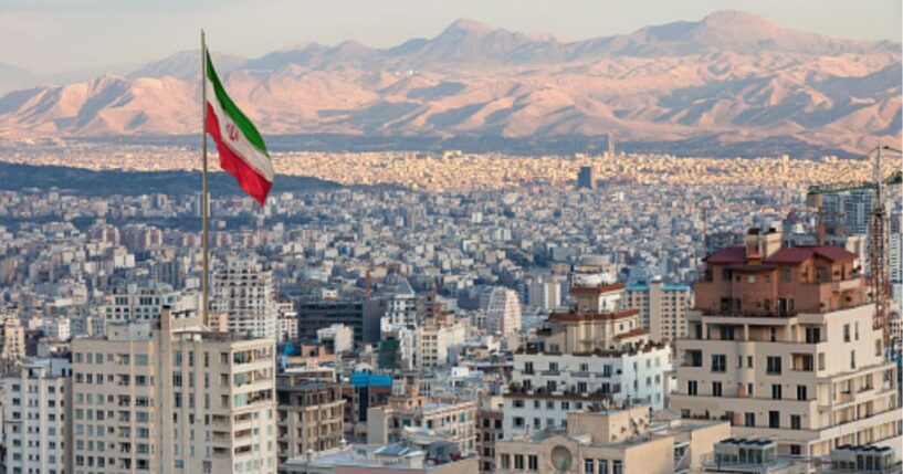 Tehran’s skyline is pictured with a large Iranian flag flying in the sky during sunset.